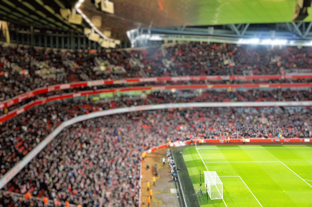 Blurred background of football players playing and soccer fans in match day on beautiful green field with sport light at the stadium.Sports,Athlete,People Concept.Emirates Stadium,Arsenal.