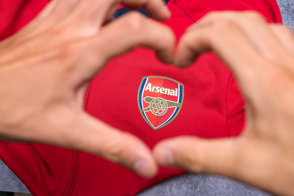 Bielsko, Poland - 08.18.2021: the supporter places his hands in the shape of a heart next to the logo of his favorite club Arsenal FC. Supporting your favorite soccer team